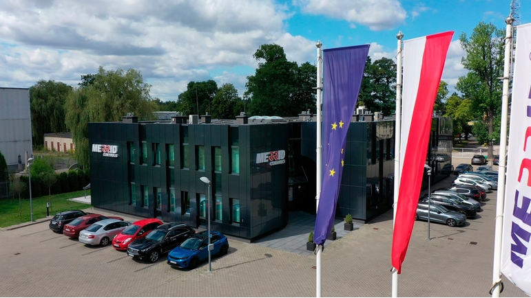 budynek z samochodami przed, siedziba firmy merrid controls, flagi na pierwszym planie