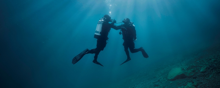 Scena podwodna: nurek wspiera drugiego nurka, który ma problemy z dopływem powietrza.