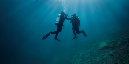 Scena podwodna: nurek wspiera drugiego nurka, który ma problemy z dopływem powietrza.