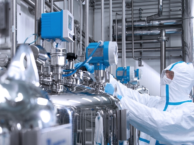 Inżynier w kombinezonie higienicznym obsługujący urządzenie w obszarze produkcji farmaceutycznej.